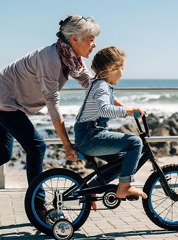 Grandmother helping girl ride a bicycle outdoors.