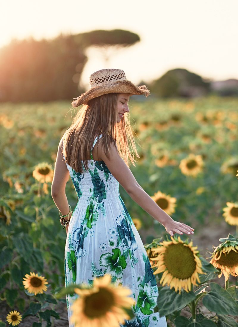 Woman in a floral dress among sunflowers.