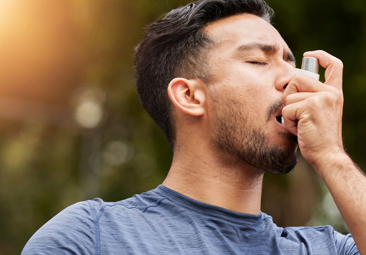 Man using asthma inhaler outdoors.